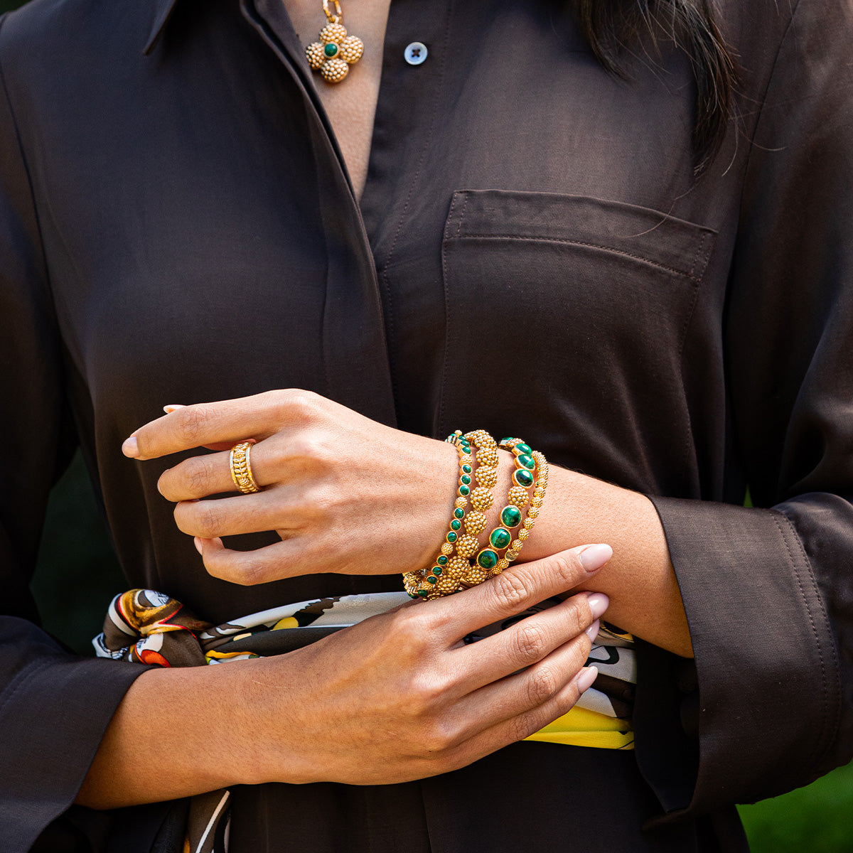 Woman wearing a Berry Gem Petite Hinged Bangle with green malachite and gold-plated berry details.