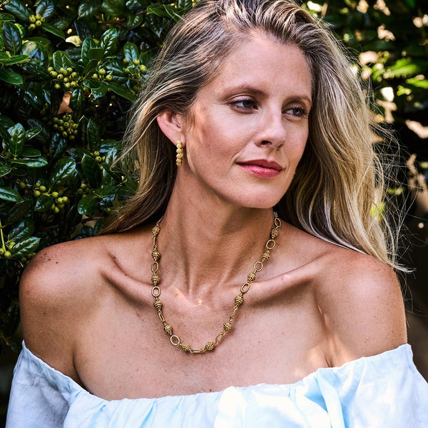 Woman wearing Berry Icon Small Hoop Earrings in gold with a matching berry motif necklace.