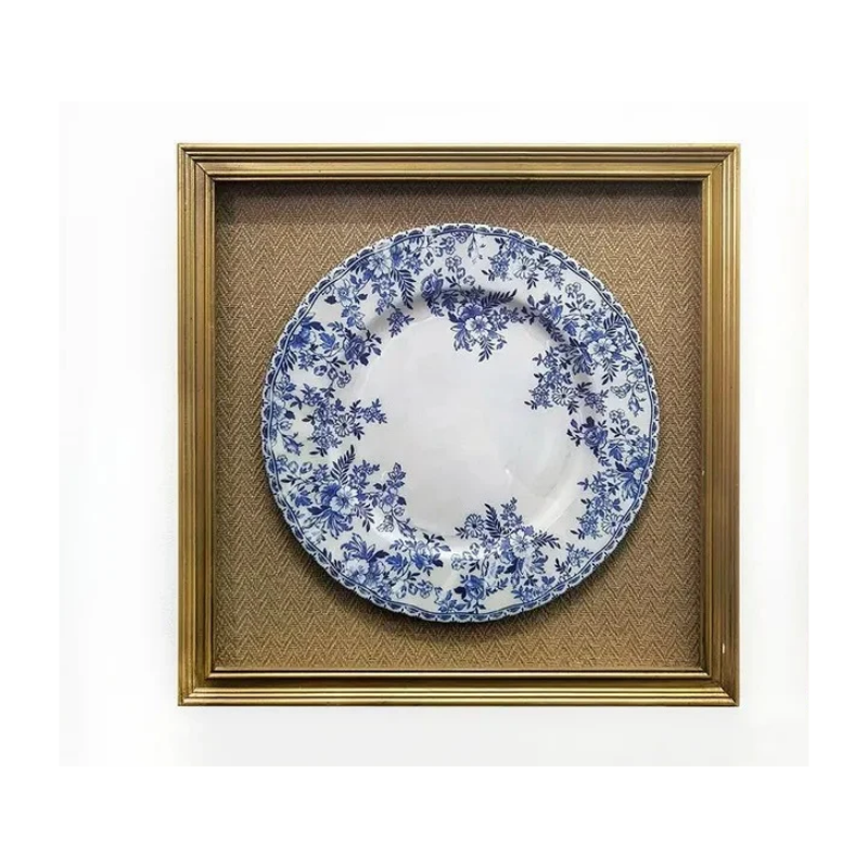Blue and white floral pattern plate mounted in a gold frame with a textured brown background.