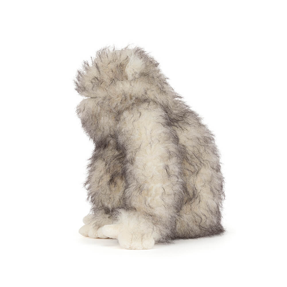 Side view of Bretti Yeti, a fluffy white and grey plush toy sitting on a white background.