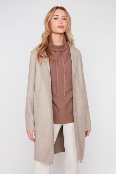 Woman wearing a heather latte brushed knit long coat with raw edges over a brown turtleneck.