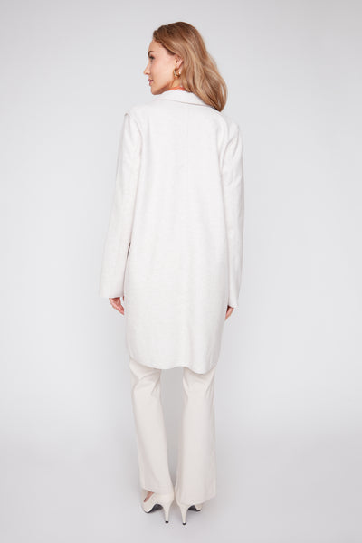 Back view of a woman wearing a long oatmeal-colored brushed knit coat with trousers and heels.