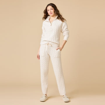 Woman wearing a cream cable knit half-zip sweater and matching tapered pants set.