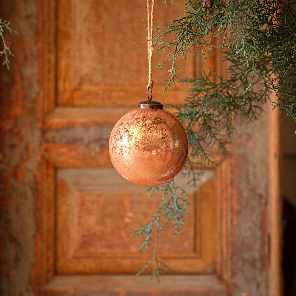 Cameo Antique Finished Glass 4" Ball Ornament hanging from a string against a rustic wooden door.