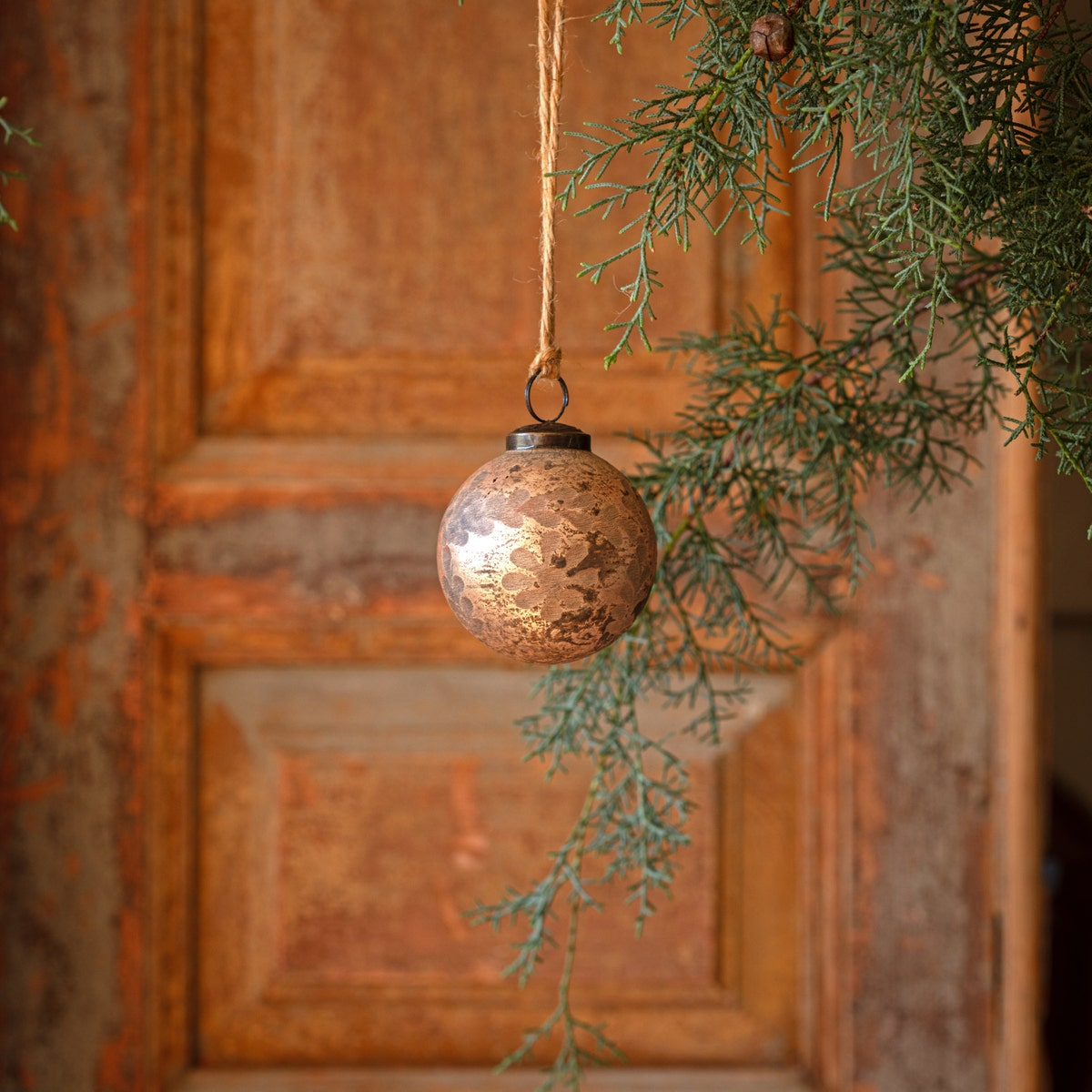 Cameo antique foil glass etched 3-inch ball ornament hanging from a twine string on a pine branch.