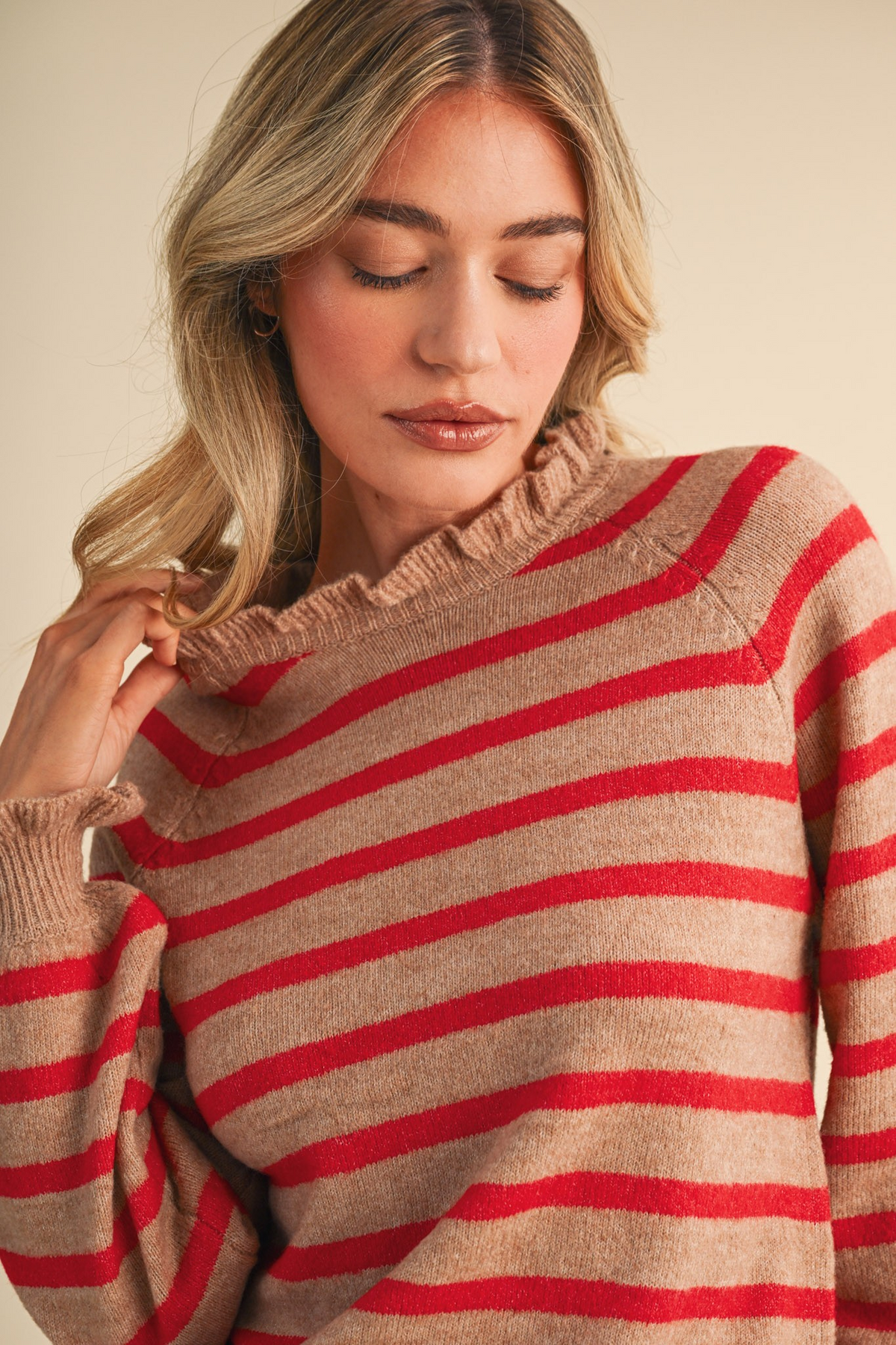 Woman wearing a desert and red striped sweater with a ruffled round neckline and raglan sleeves.