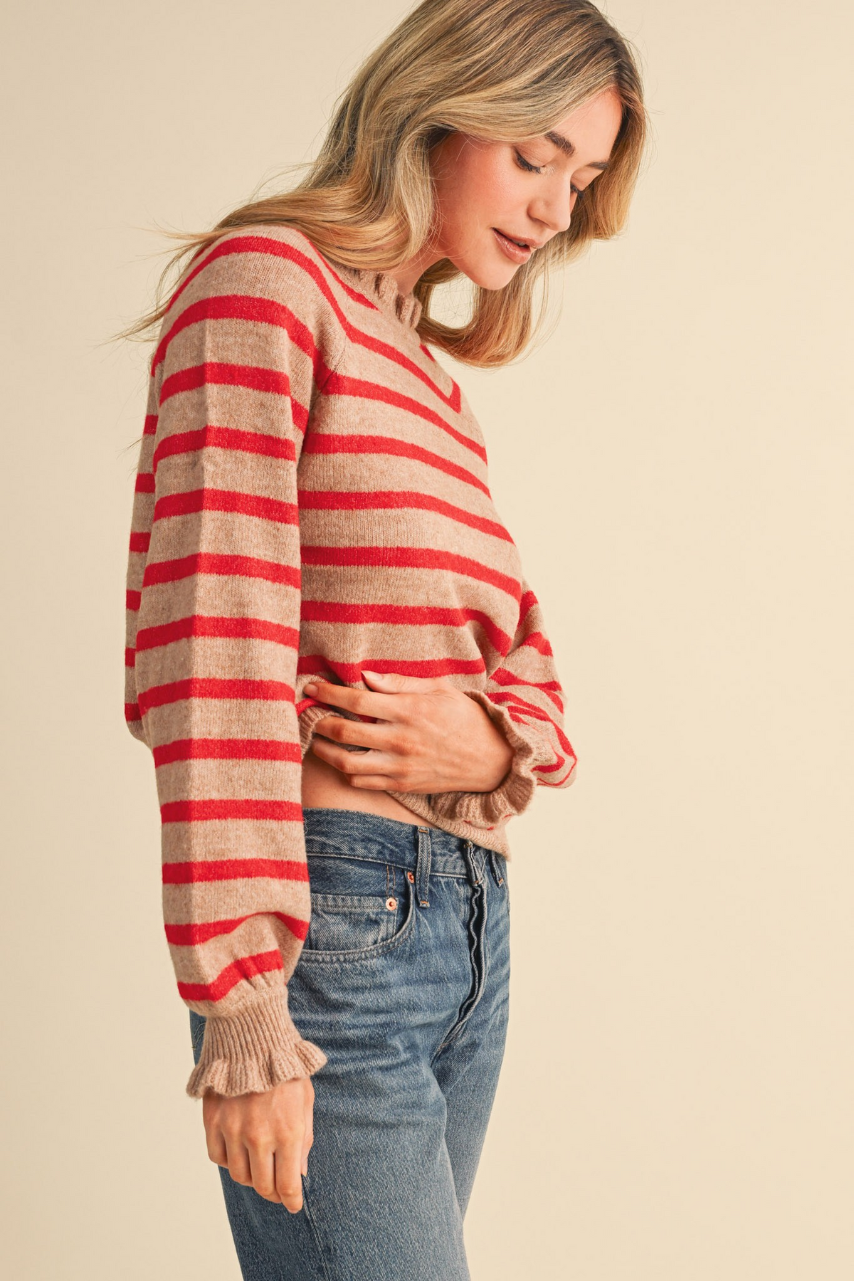 Woman wearing the Charlie Ruffled Striped Sweater in desert and red with blue jeans.
