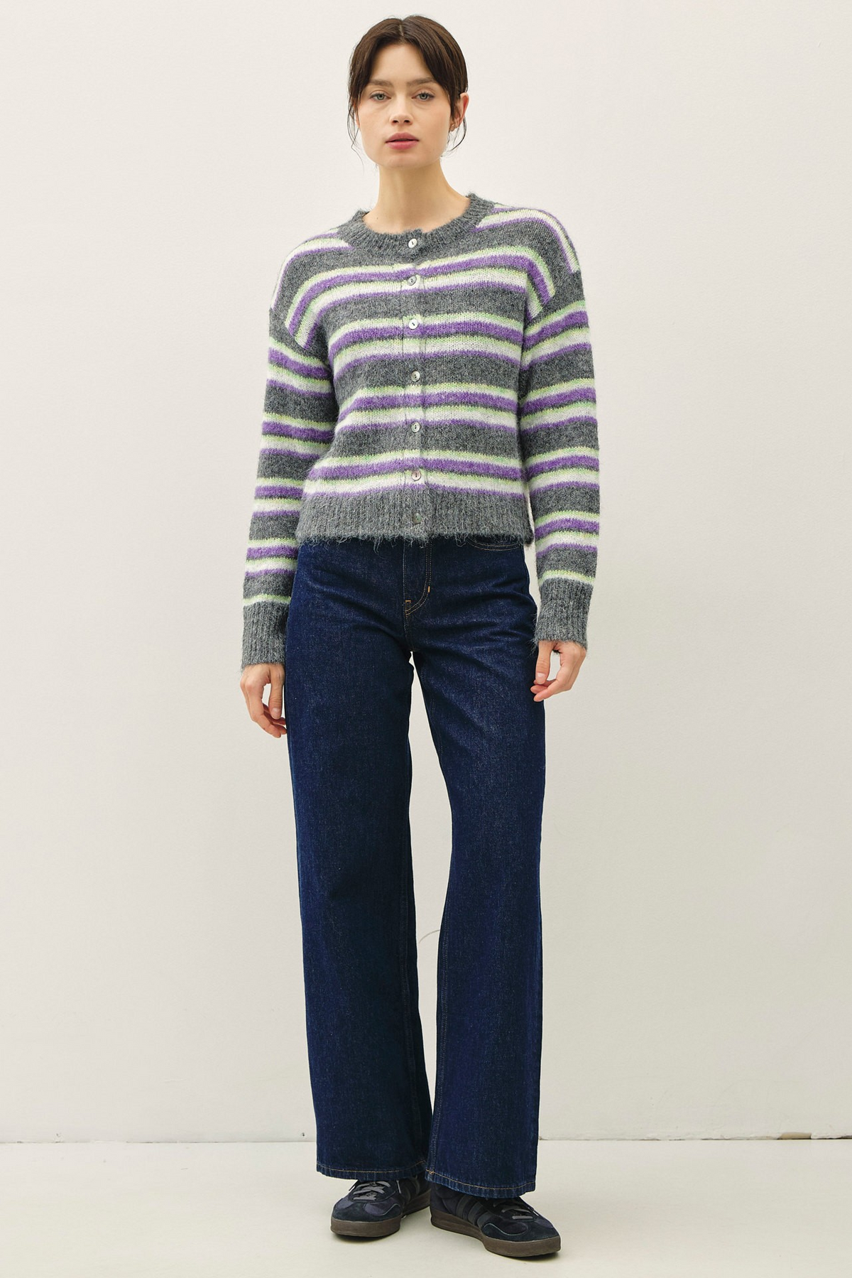 Woman wearing a grey, purple, and green striped fuzzy knit cardigan with dark blue wide-leg jeans.