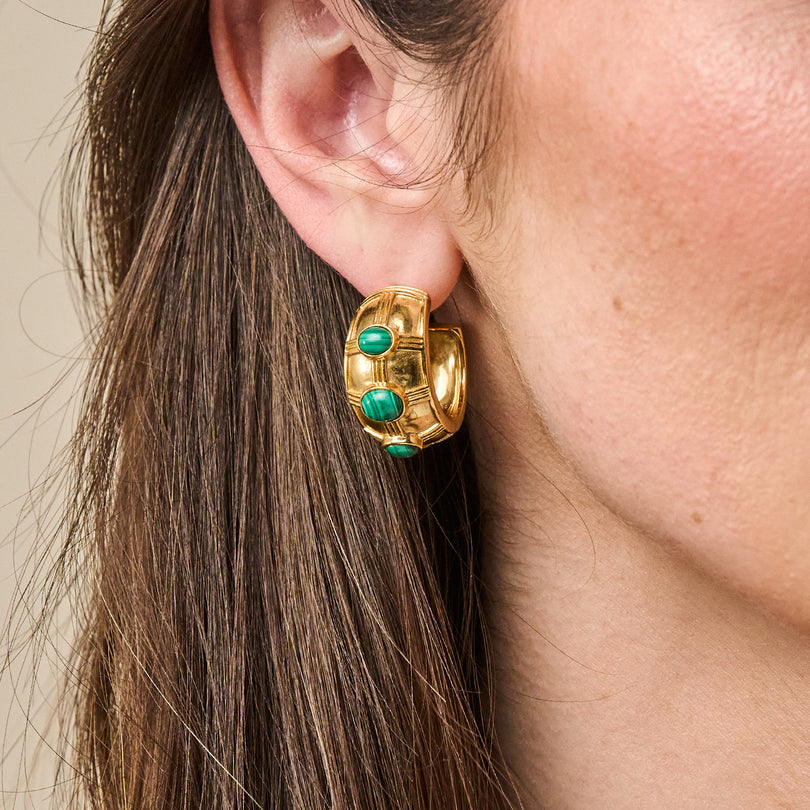 A person wearing a thick gold hoop earring featuring three green malachite stone cabochons.
