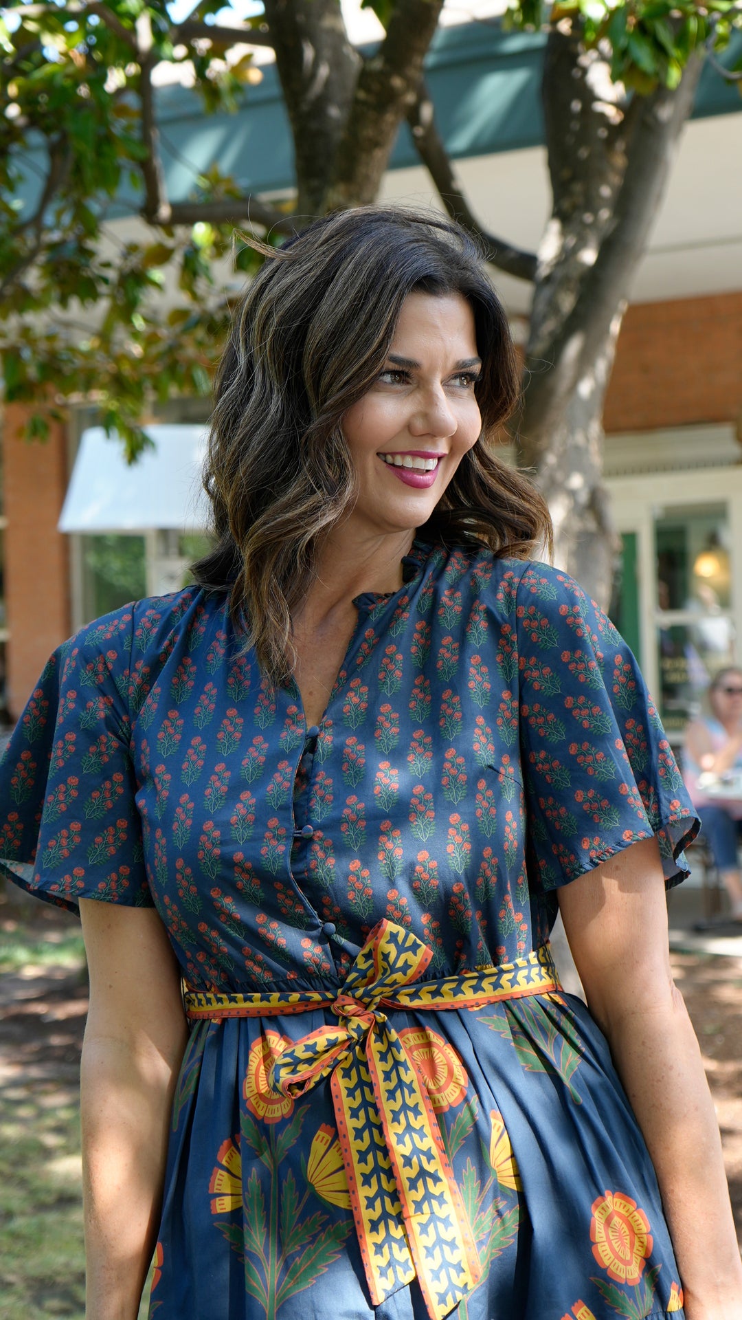 Woman wearing the Chloe Floral Button Down Dress with a patterned tie belt and short sleeves.