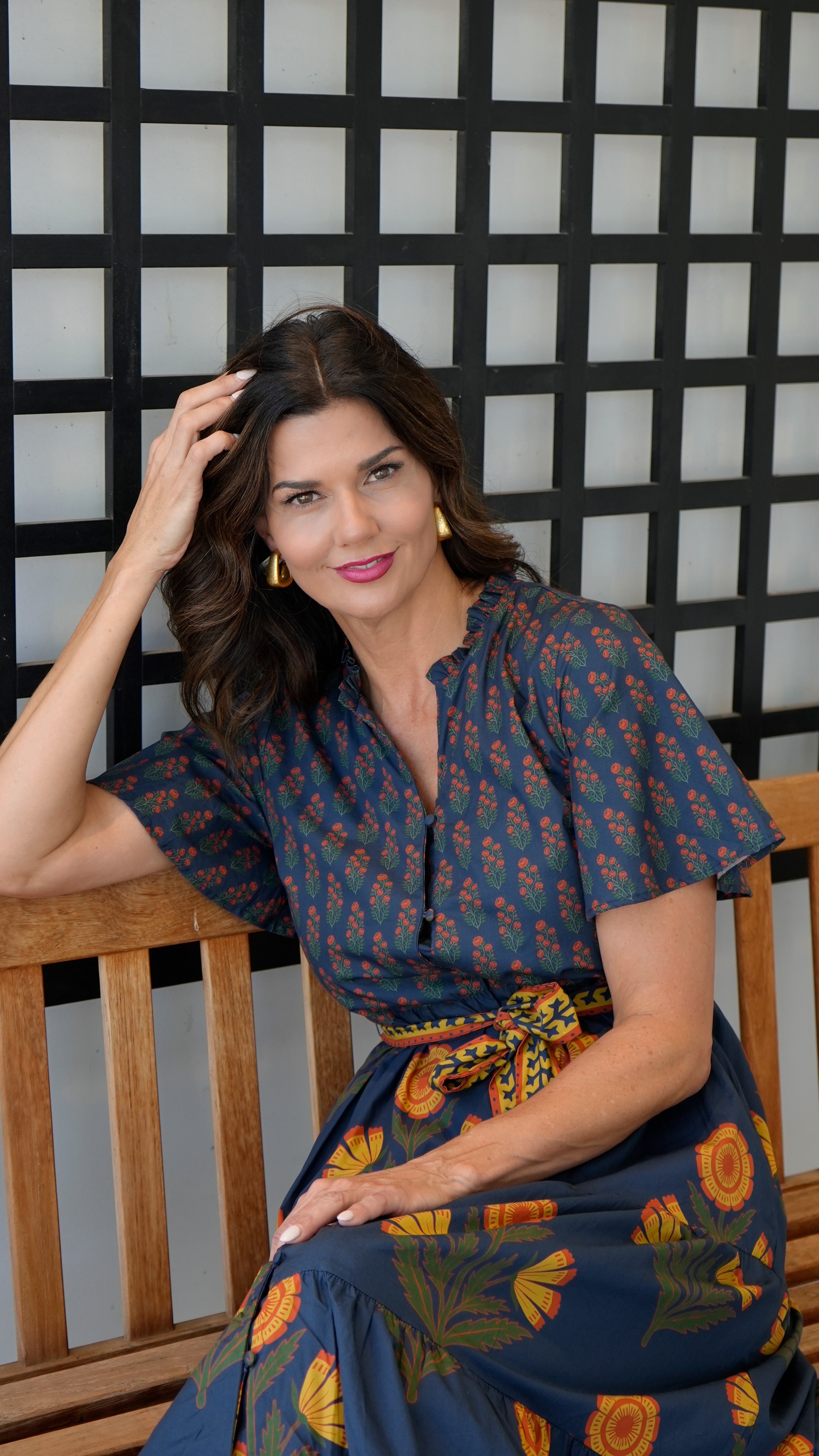 Woman wearing the Chloe Floral Button Down Dress with a tie belt, sitting on a wooden bench.