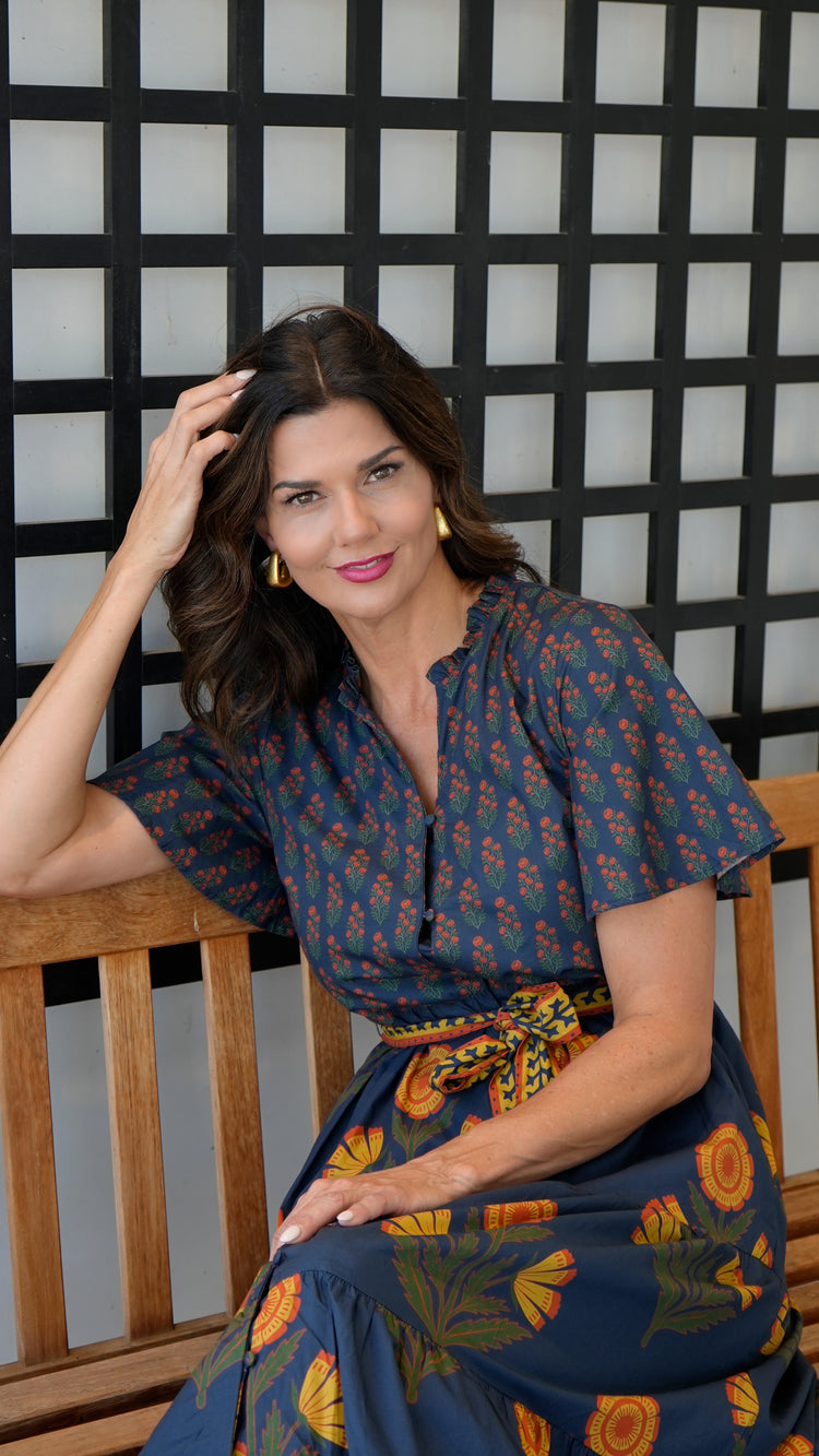 Woman wearing the Chloe Floral Button Down Dress with a tie belt, sitting on a wooden bench.