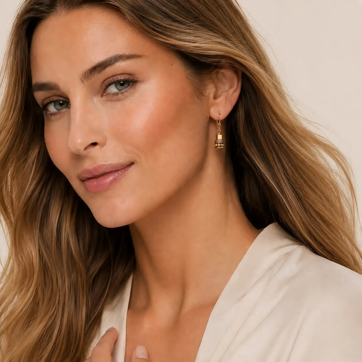 Woman wearing Urban Nature Cube earrings in beige and gold with leverback closure.