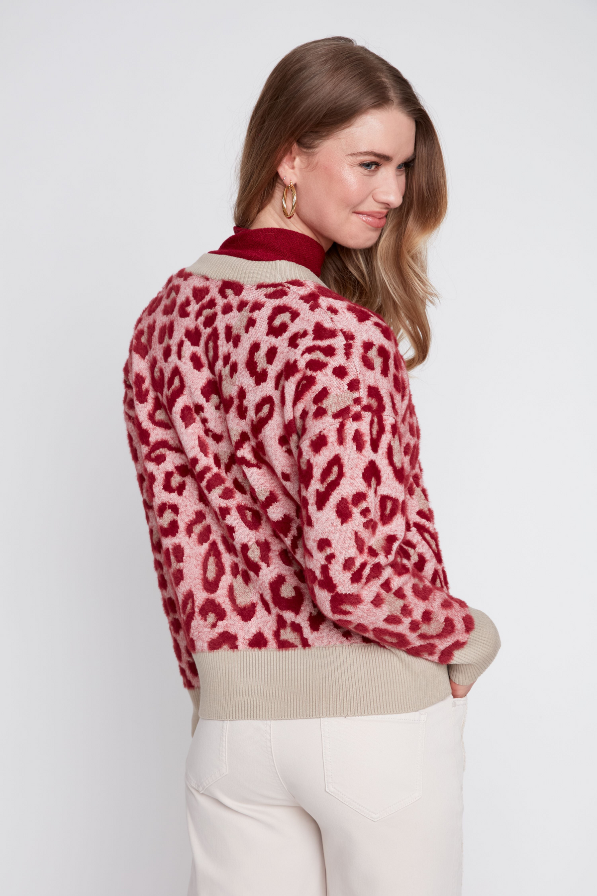 Back view of a woman wearing a pink and red leopard print jacquard knit cardigan with beige trim.