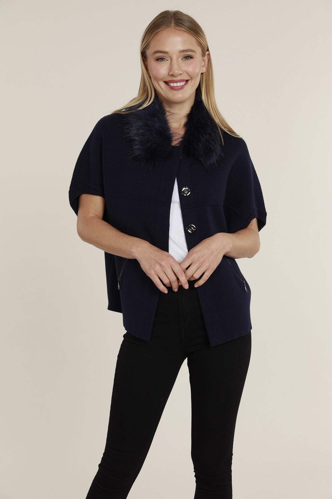 Woman wearing a navy blue short-sleeve cardigan with a matching faux fur collar and snap closures.