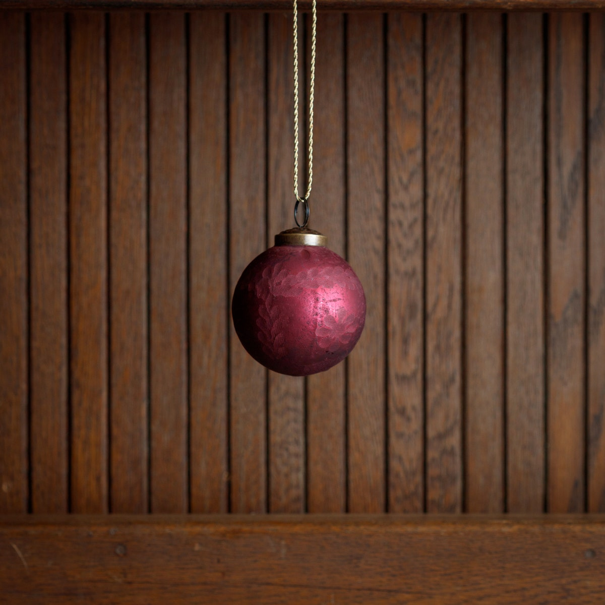 3-inch frosted cranberry etched glass ball ornament hanging against a wood paneled background.