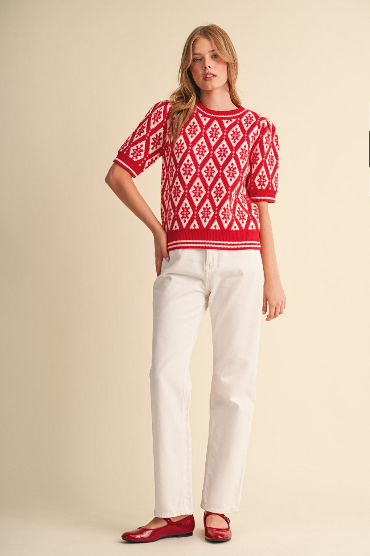 Woman wearing the Isabella red and ivory geometric knit short sleeve sweater with white pants.