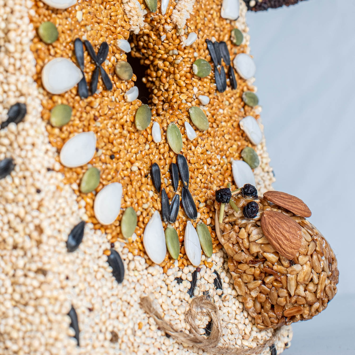 Close-up of a birdhouse clock face made of seeds with a small seed-covered mouse on the side.