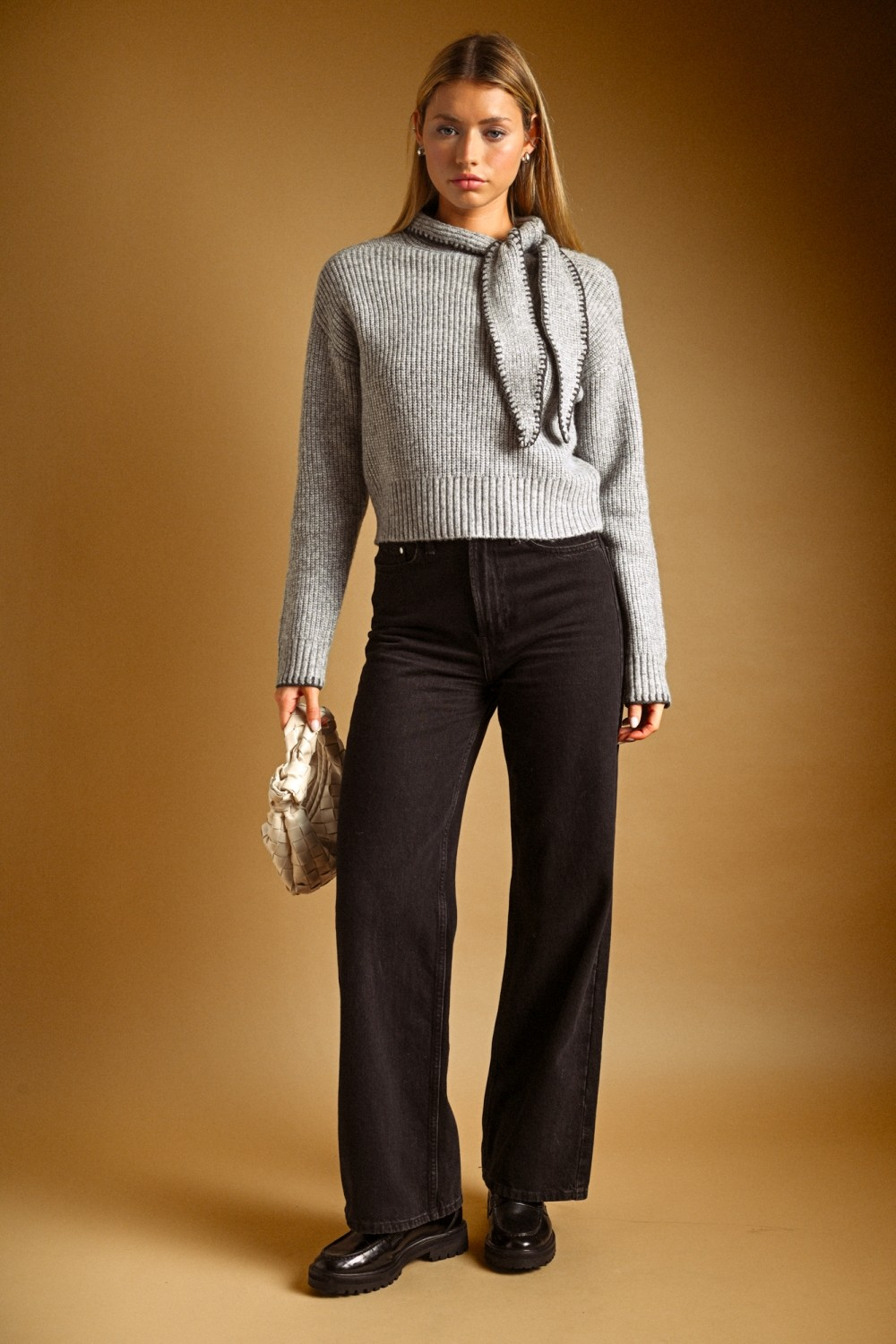 Woman wearing the Sofia High Neck Tied Neck Sweater in light gray with black wide-leg jeans.