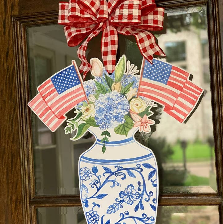 Patriotic door hanger featuring a blue and white floral vase with American flags and a red bow.