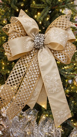 Ivory and gold velvet holiday bow with a rhinestone center knot on a lit Christmas tree.