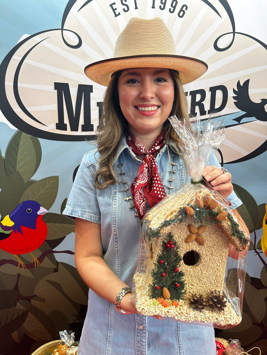A woman holding a Juniper B&B birdhouse decorated with seeds, almonds, and a small Christmas tree.
