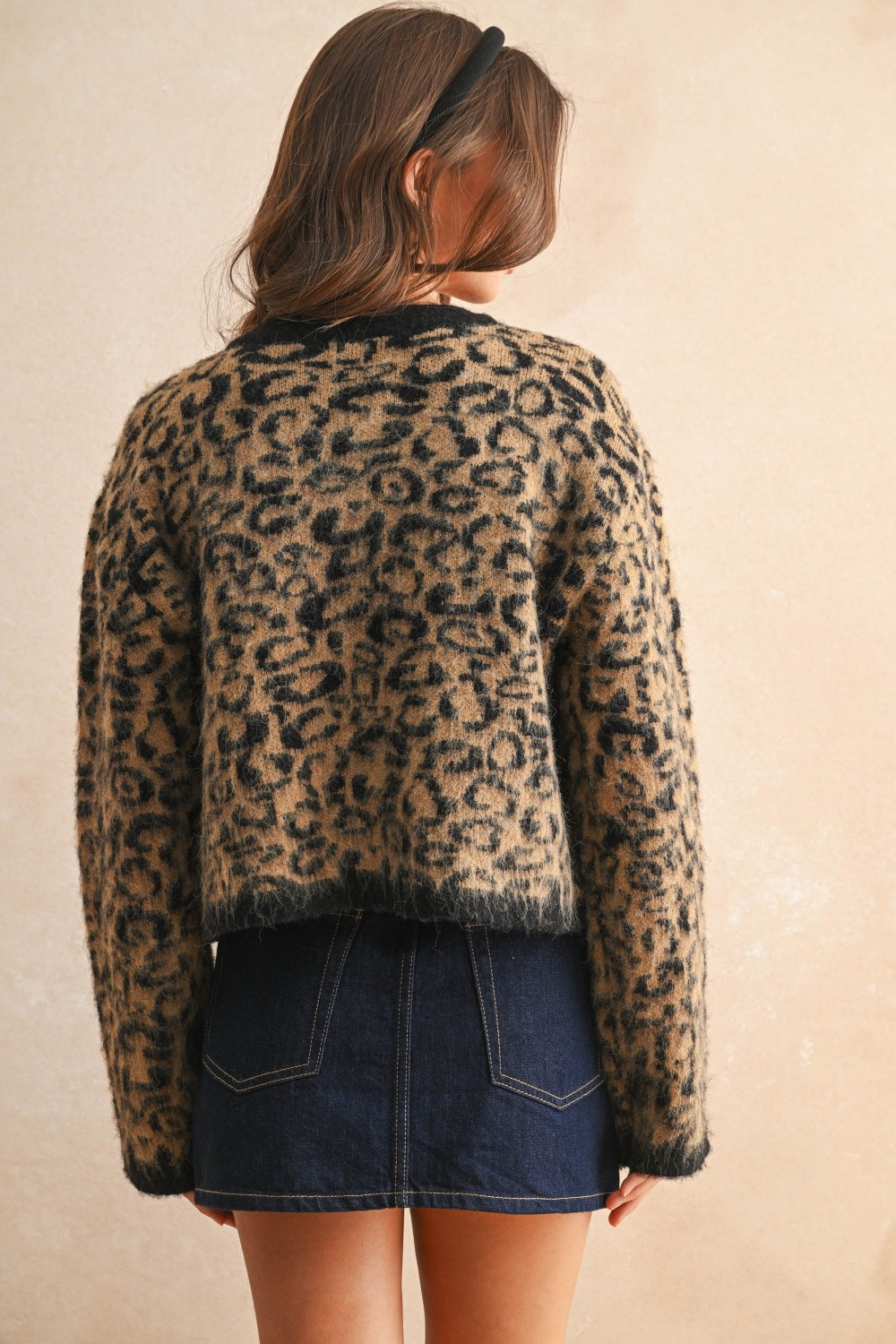 Back view of a woman wearing a cropped leopard print fuzzy knit cardigan and a denim skirt.