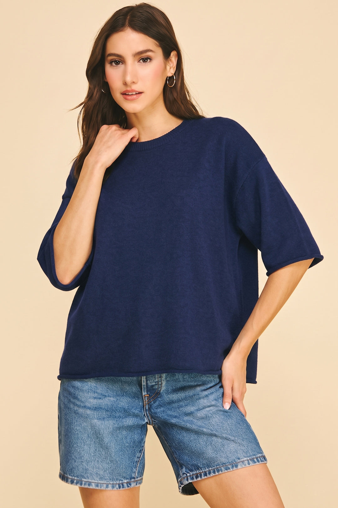 Woman wearing a navy Lilyana oversized short sleeve knit sweater with blue denim shorts.