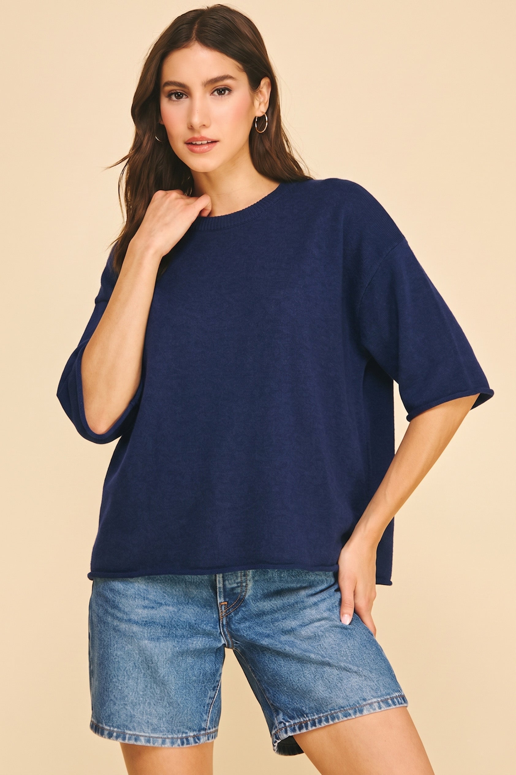 Woman wearing a navy Lilyana oversized short sleeve knit sweater with blue denim shorts.