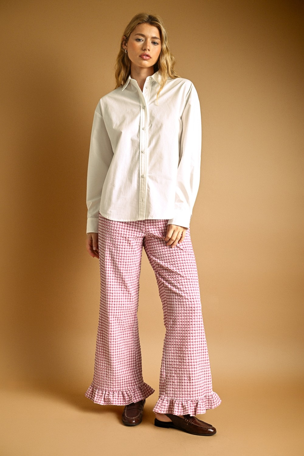Woman wearing a white Eunice oversized long sleeve button-down shirt with pink gingham trousers.