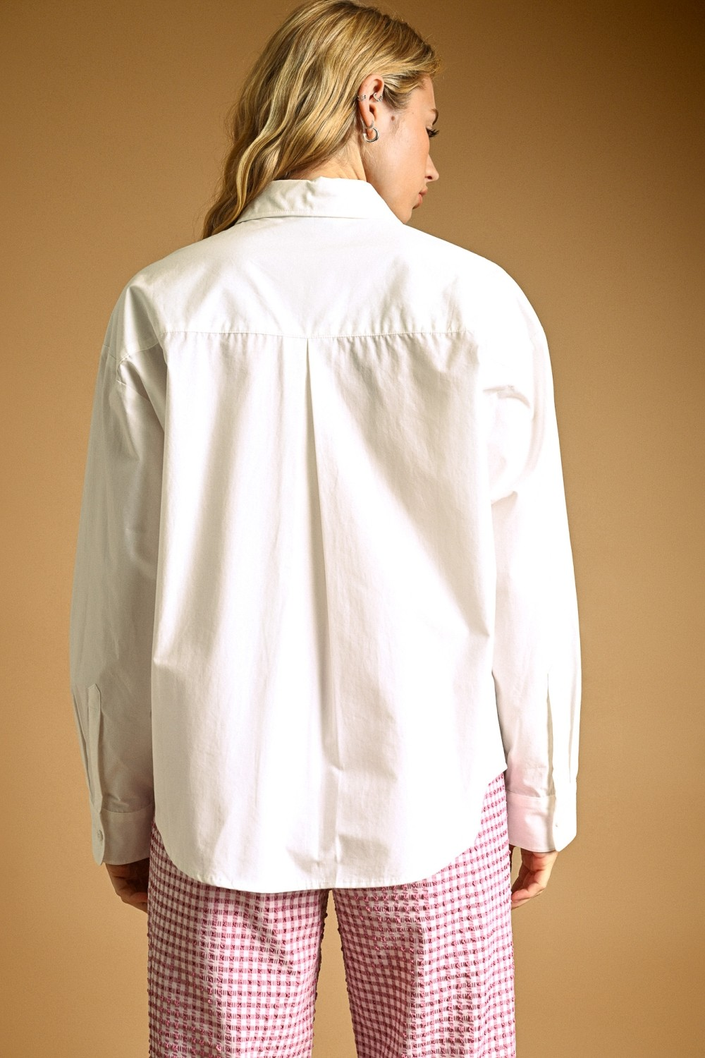 Back view of a woman wearing a white oversized long sleeve button-down shirt with a curved hem.