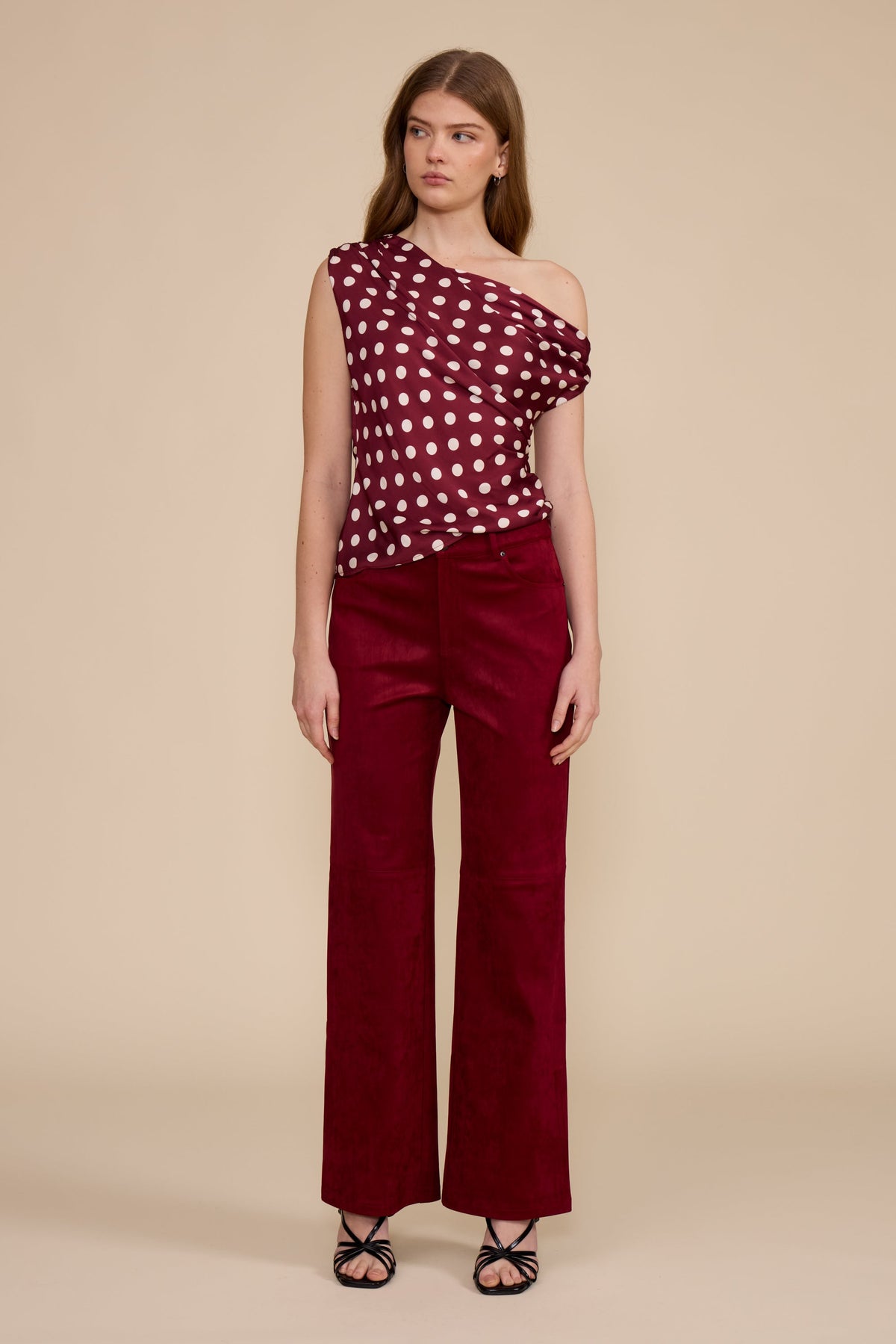 Woman wearing deep merlot Vea faux suede wide-leg pants and a polka dot one-shoulder top.