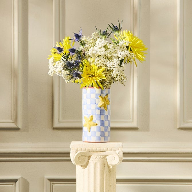 Hand-painted blue and white checkered vase with yellow stars holding a bouquet on a stone pedestal.