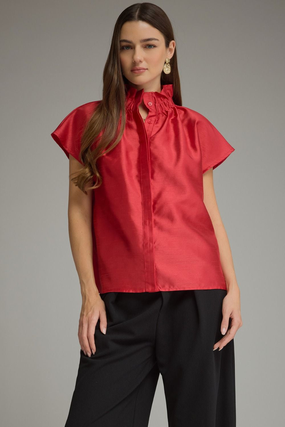 Woman wearing a red Maya solid cap sleeve top with a ruffled high neckline and black trousers.