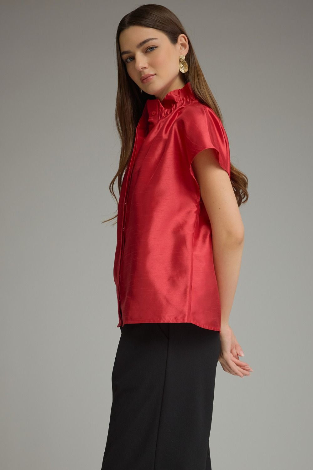 Woman wearing a red Maya solid cap sleeve top with a ruffled high neckline and black trousers.
