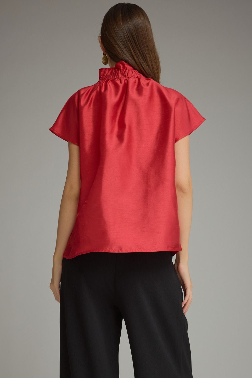Back view of a woman wearing a red Maya cap sleeve top with a ruffled high neckline and black pants.