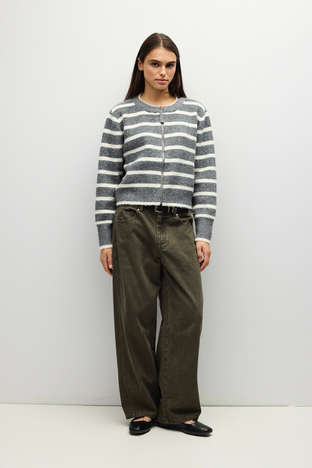 A woman wearing the Natalia Sweater, a grey and white striped boucle zip-up with olive wide-leg pants