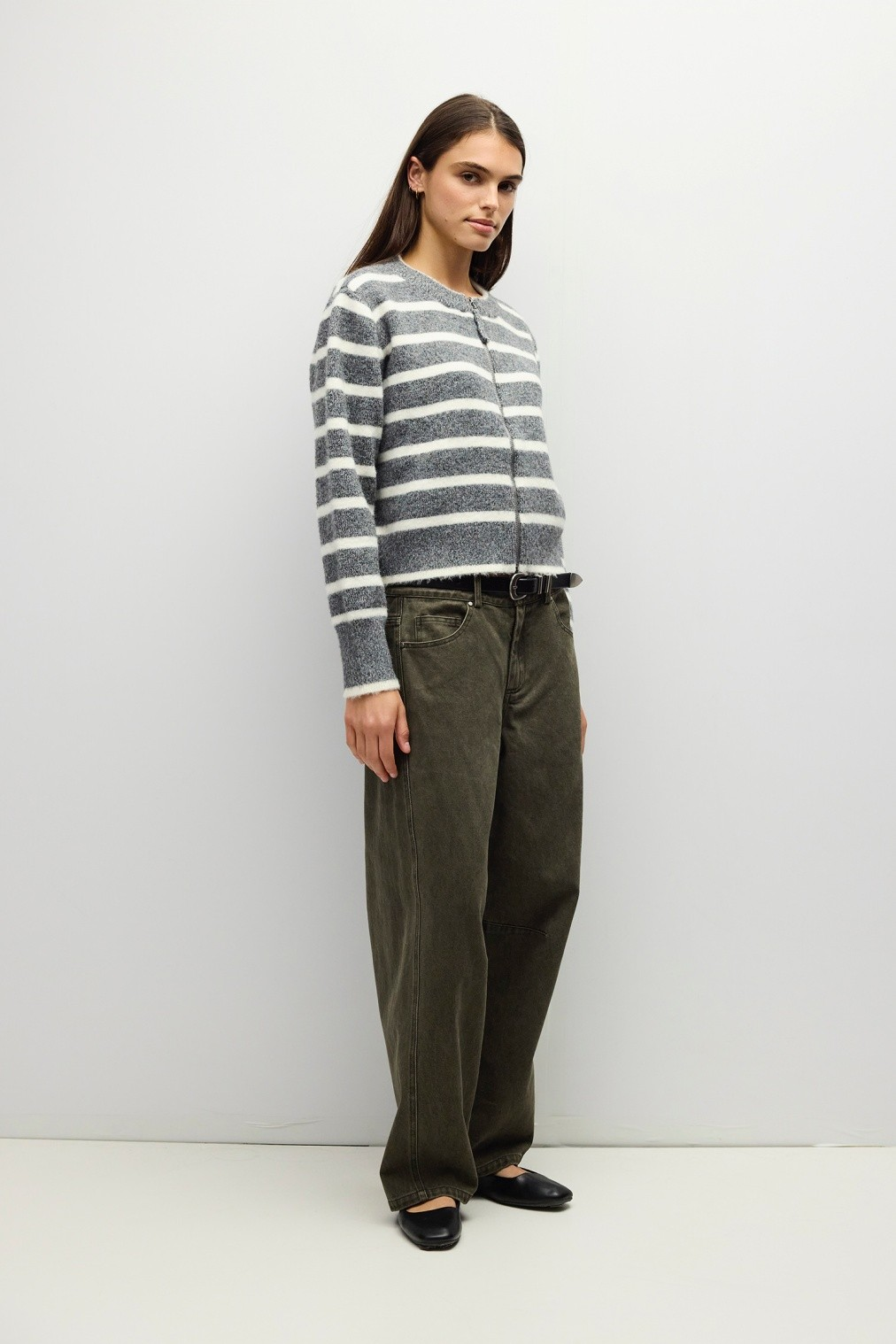 Woman wearing the Natalia Sweater, a grey and white striped zip-up boucle knit with olive pants.