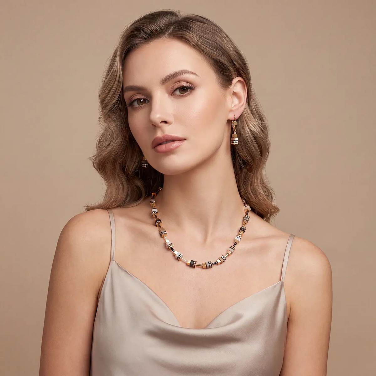 Woman wearing the Urban Nature Cube necklace in beige-gold with matching cube earrings.