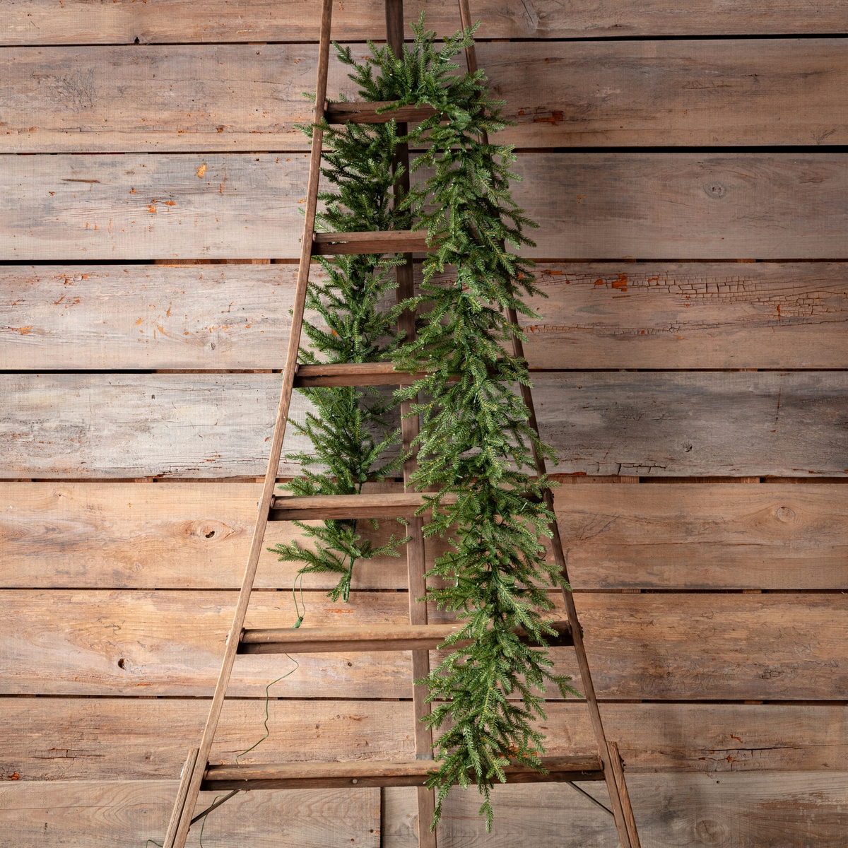 Olympia Fir 9 Ft Garland with dense evergreen branch tips draped over a rustic wooden ladder.