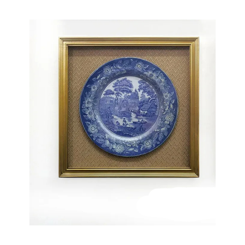 Blue and white pastoral landscape plate print in a gold frame with a textured tan mat.