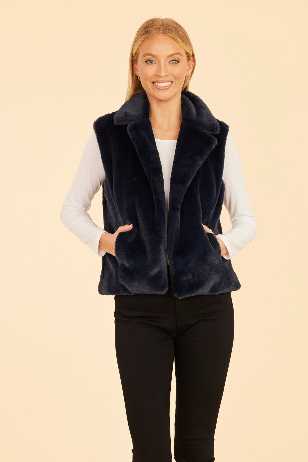 Woman wearing a navy blue Naomi plush faux fur notch collar vest over a white long-sleeve top.