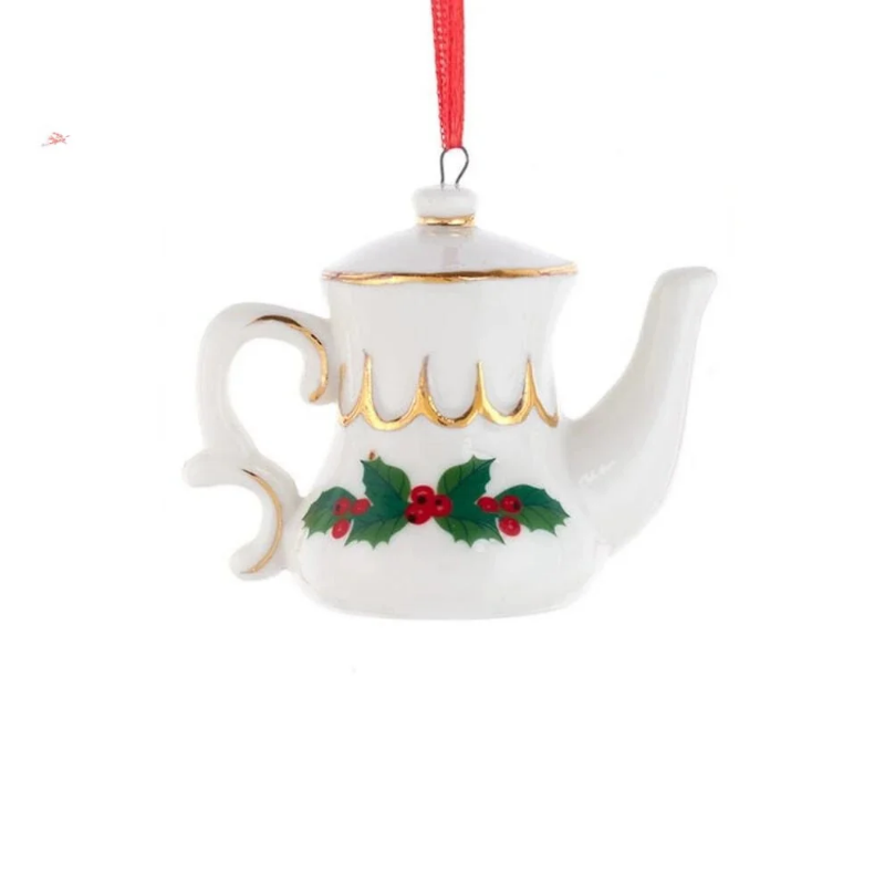 White porcelain teapot ornament with gold trim and holly berry design hanging from a red ribbon.