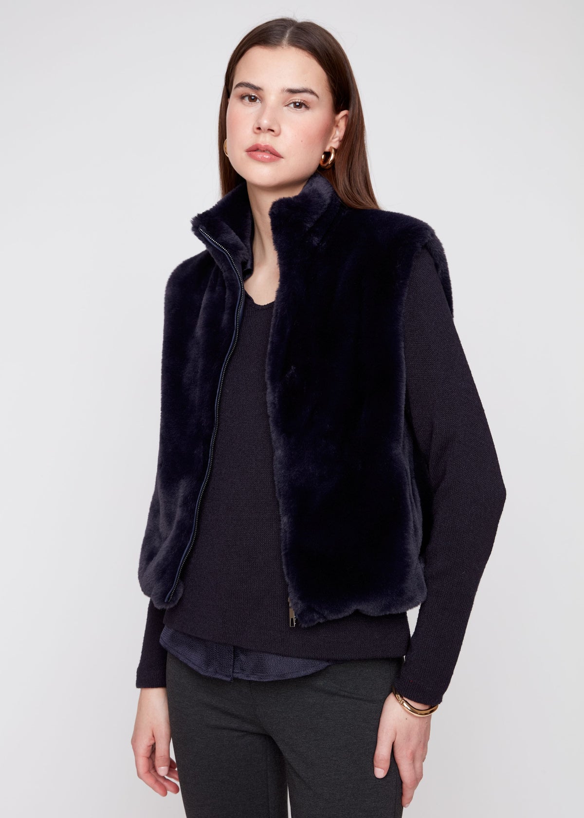 A woman wearing the Ella Solid Faux Fur Short Vest in midnight blue over a dark sweater and pants.