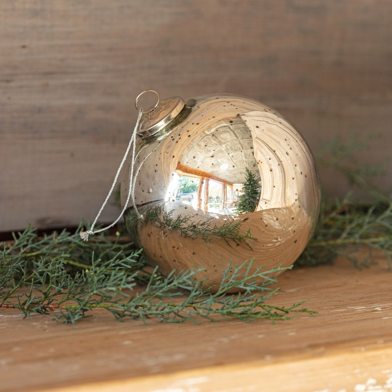 Round 6-inch antique silver mercury glass ball ornament on a wooden surface with greenery.