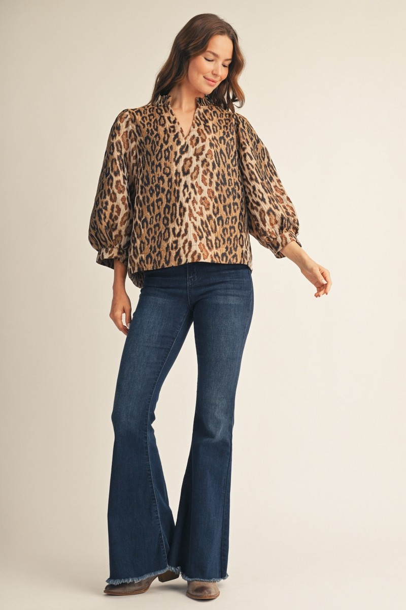 Woman wearing the Eliana Ruffled Neck Leopard Jacquard Top with flared blue jeans.