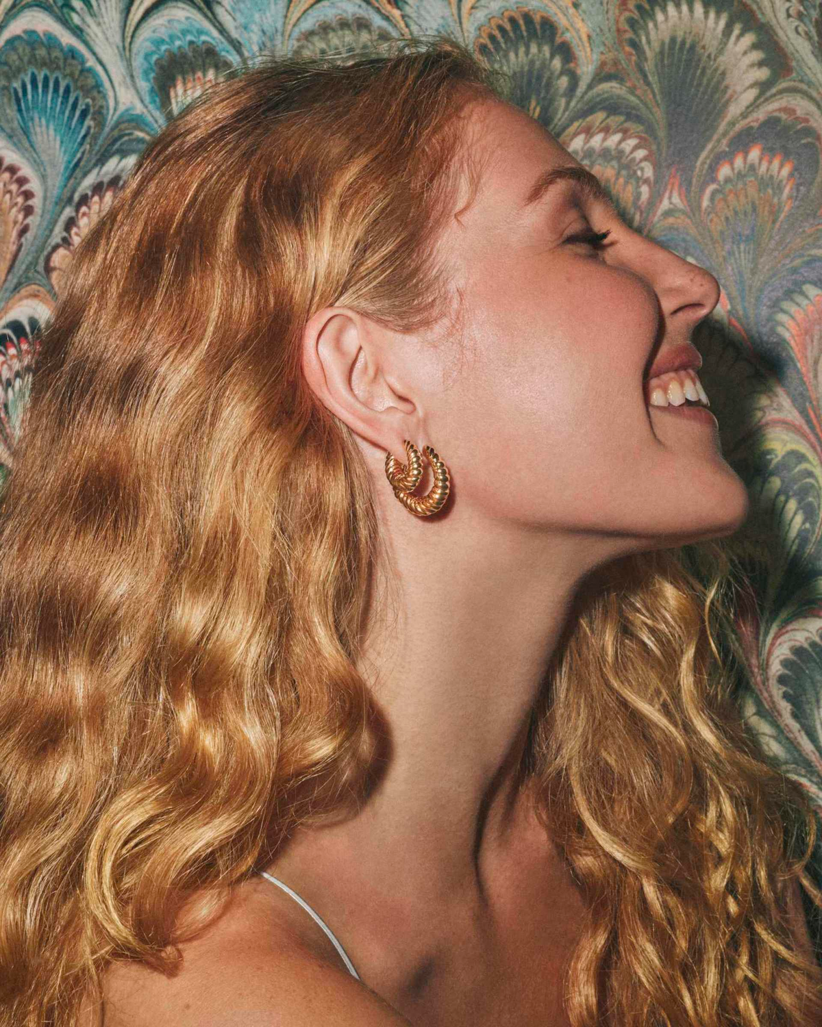 A woman wearing the gold Sandy Hoop Earrings, featuring a textured, sculptural twisted design.