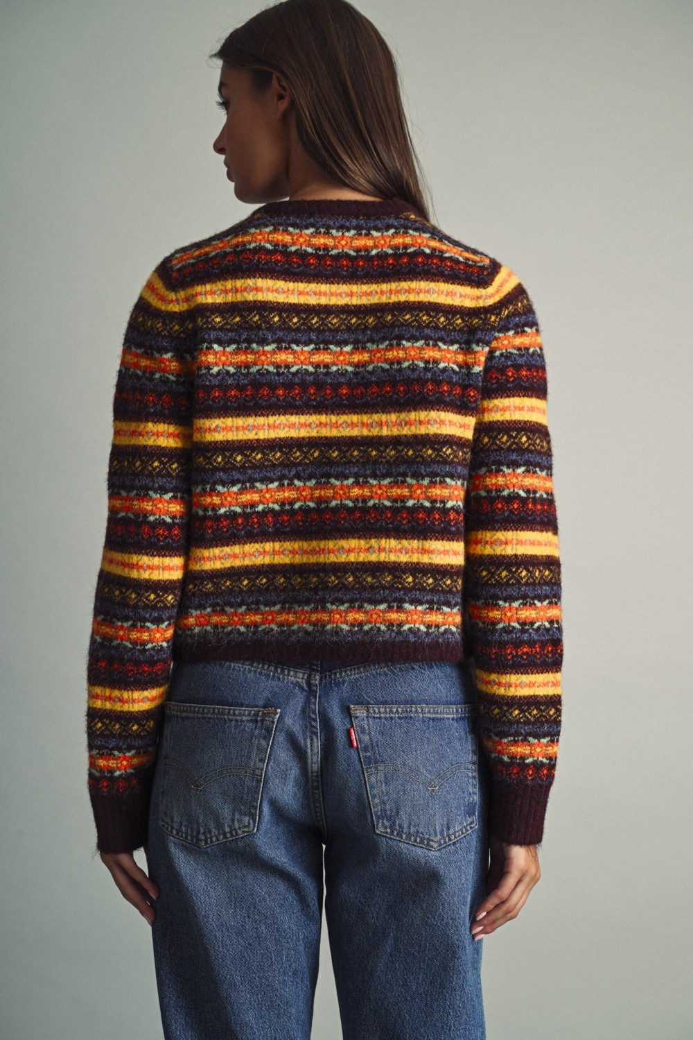 Back view of a woman wearing a multicolored Fair Isle pattern cropped knit sweater and blue jeans.