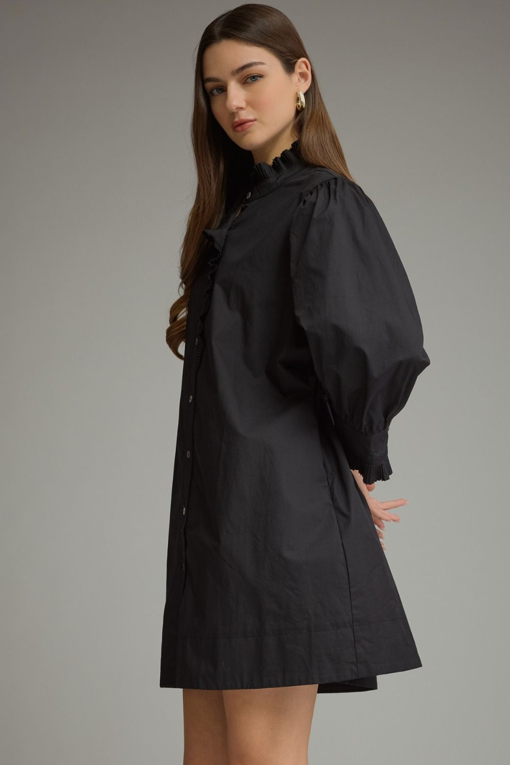 Woman wearing the Agnes black mini dress with 3/4 puff sleeves and a ruffled high neckline.