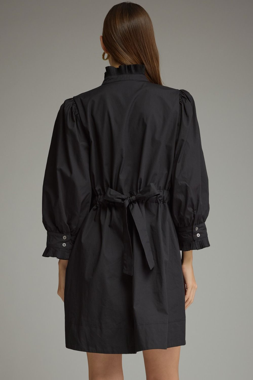 Back view of a black Agnes mini dress with 3/4 puff sleeves, a ruffled collar, and a tie-back waist.